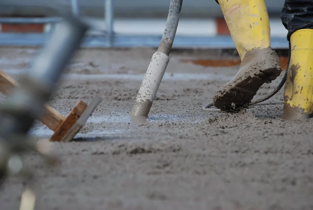 Betonarbeiten auf der Baustelle: Gummistiefel und Rüttelflasche im frischen Beton